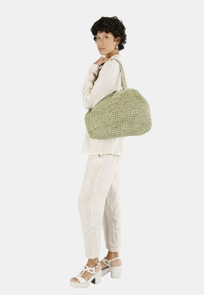 Geweven groene handtas met een ronde, gestructureerde vorm en een textuurfinish. Gecombineerd met een lichtbeige, gestreept outfit en witte hoge sandalen.