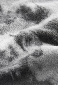 Tissu en laine gris doux avec une texture duveteuse présentant des motifs abstraits foncés et des plis délicats.