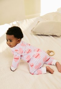 Pigiama a quadretti viola e bianchi con grandi cuori rosa e la scritta "I love my DADDY." Bambino gattona su una coperta a righe chiare.