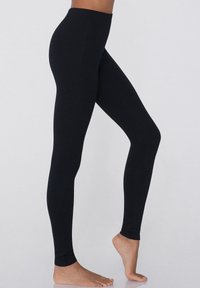 Leggings noirs avec une taille haute, texture lisse, coupe ajustée et sans coutures visibles, s'étendant jusqu'à la cheville.