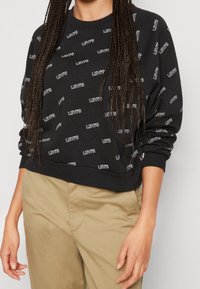 Felpa nera con motivo del logo "LEVI'S" bianco, scollo tondo e maniche lunghe. Vestibilità casual con polsini e orlo a costine.
