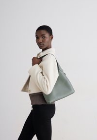 Green leather tote bag with a smooth texture and minimalistic design, featuring a single strap and rounded edges.