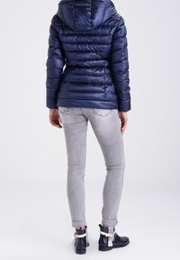 Doudoune bleu marine à capuche, design matelassé et texture brillante. Associée à un jean skinny gris clair et des bottines à pompons.