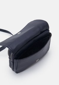 Námořnická kožená kabelka přes tělo se zipovým otevíráním, která má texturovaný povrch, kovové detaily a vzorované látkové vnitřnosti.