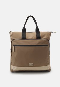 Bruine tote bag gemaakt van duurzaam stof, met een voorzak met rits, twee zwarte stoffen handvatten en een crèmekleurige onderaccent.