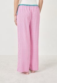 Różowe spodnie o szerokich nogawkach z wzorzystym deseniem, na którym znajdują się małe niebieskie motywy kwiatowe oraz turkusowy elastyczny pas. Miękka tekstura materiału.