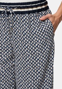 Navyfarbene Hose mit Rautenmuster in Weiß, Beige und Hellblau. Verfügt über einen Kordelzugbund und seitliche Taschen.