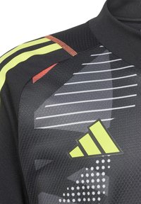 Zwarte sporttrui met gele en rode accenten, geometrische patronen en een groot geel logo met drie strepen aan de linkerkant.