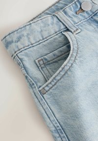 Jasnoniebieskie dżinsy z denimu z przednią kieszenią, srebrnym guzikiem oraz kontrastującym brązowym przeszyciem. Teksturowana tkanina z wyblakłym wykończeniem.