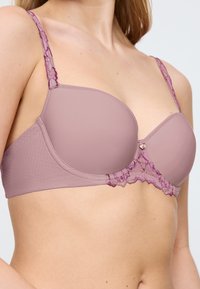 Mauve vadderad bh med delikat spetsdetalj, med en texturerad yta och justerbara band. Liten dekorativ hårdvara i mitten.