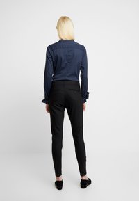 Chemise à manches longues navy avec détail de couture au dos, associée à un pantalon noir ajusté ; texture de tissu lisse, design minimaliste et sans motifs visibles.