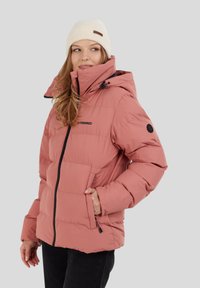 Chaqueta acolchada rosa con cierre de cremallera y capucha, que presenta un logo negro y bolsillos laterales. Textura suave y acolchada, combinada con un gorro de punto color crema.