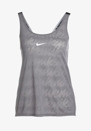 Kobieta ubrana w szary top bez rękawów, czarne legginsy Nike z subtelnym wzorem oraz jasnoróżowe sneakersy Nike, stoi z rękami za plecami.