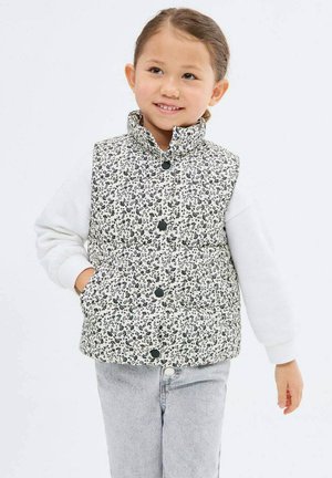Zateplená vesta s čierno-bielym kvetinovým vzorom, vysokým golierom, patentkami a dvoma bočnými vreckami, nosená cez bielu košeľu s dlhým rukávom.