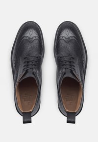 Scarpe di pelle nera con una finitura testurizzata, design wingtip, chiusura con lacci e interno marrone a contrasto. Inclusa una linguetta per il tiraggio.