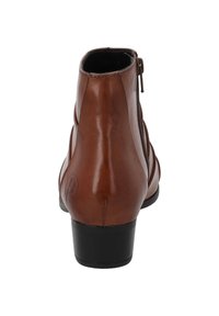 Botín de cuero marrón hasta el tobillo con textura suave, cremallera lateral y un tacón negro bajo. Presenta un detalle de logotipo circular en el tacón.