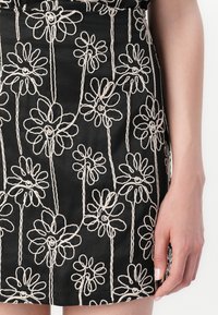Svart kjol med blommönster i krämfärg, med konturerade blommor och stjälkar, som visar en slät textur.