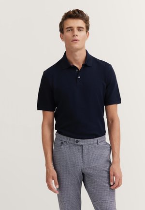 Navy blue polo shirt with a textured pattern, short sleeves, and a two-button placket, paired with light gray checkered trousers.