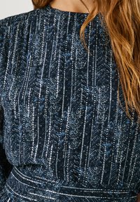 Marinblå klänning i tyg med vertikala silver- och blå blommönster; har en rynkad halsringning och texturerad yta.