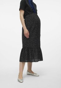 Jupe de maternité noire à pois avec une hem ruffled et une taille élastique. Portée avec un top noir et des ballerines argentées.