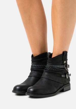 Mustat nilkkurit, jotka on valmistettu nahasta ja joissa on vetoketjusuljenta, punottu hihna ja metalliset yksityiskohdat, matalalla tukevalla korolla.