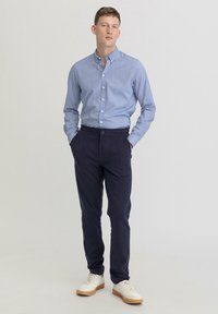Lichtblauw overhemd met lange mouwen, gecombineerd met marineblauwe chinos en witte sneakers met beige zolen. Eenvoudig, gestroomlijnd ontwerp.