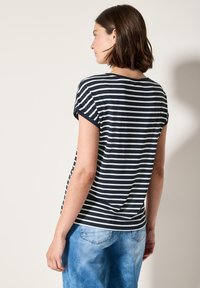 T-shirt rayé bleu marine et blanc avec des manches courtes retroussées, en tissu doux et à coupe décontractée, associé à un jean en denim bleu clair.