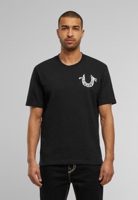 Zwart katoenen t-shirt met korte mouwen, voorzien van een witte logoprint op de linkerkant van de borst. Klassiek ronde hals ontwerp, met een gladde textuur.