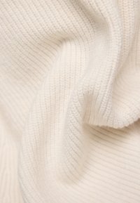 Cremfarbener Strickstoff mit geripptem Muster, das weiche und leicht flauschige Fasern zeigt und sanfte Falten und Kurven bildet.