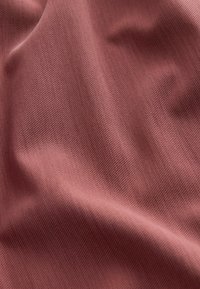 Close-up van zachte, gladde stof met diagonale weefpatroon in een gedempte stofroze kleur, met zachte plooien en textuurdetails.