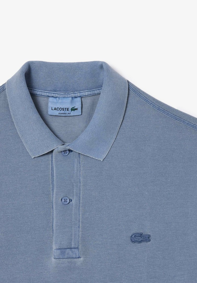 Polo de algodón azul con tejido texturizado, dos botones, cuello con solapa y un logo bordado en el pecho. Diseño de ajuste clásico.