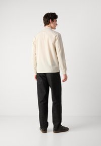 Lys beige knapp-up skjorte med lange ermer, kombinert med mørke denimbukser. Skjorten har et minimalistisk design og en subtil teksturert finish.
