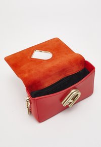 Röd läderväska med ett guldmetallspänne och orange mockainredning. Har ett unikt utskuret handtag och en svart tygfoder.