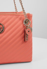 Sac à main matelassé corail avec une anse chaîne. Doté de ferrures dorées et d'une étiquette logo. L'extérieur présente des coutures diagonales pour la texture.