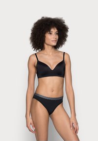Set di lingerie nera caratterizzato da un reggiseno con finitura liscia e opaca, scollatura a V e slip a bikini abbinati con una cintura a pois.
