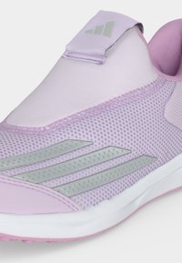 Αθλητικό παπούτσι slip-on ανοιχτού μοβ χρώματος με ανοιχτό πάνω μέρος από δίχτυ, τρεις ανακλαστικές ρίγες στο πλάι και μαλακό άσπρο πάτο με ροζ εξωτερική σόλα.