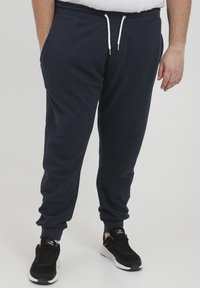 Navy Jogginghosen aus weichem Baumwollmix, mit elastischem Bund, Kordelzug und schmalen Beinen. Mit Seitentaschen gestaltet und mit schwarzen Sneakers kombiniert.