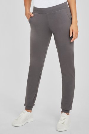 Gray, tapered sweatpants made of soft fabric with an elastic waistband, side pockets, and cuffed ankles. Worn with white sneakers.
