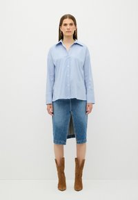 Camicia a righe blu e bianche con bottoni, a maniche lunghe, abbinata a una gonna di jeans fino al ginocchio con uno spacco frontale. Stivali alla caviglia in suede marroni.