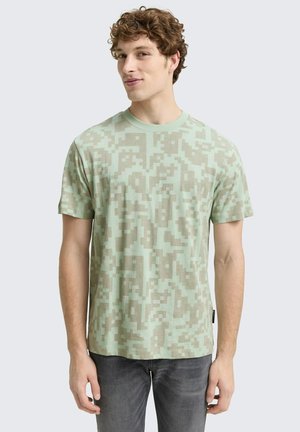 Light green t-shirt with a digital camouflage pattern in varying shades of green and beige. Short sleeves, round neckline, cotton material.