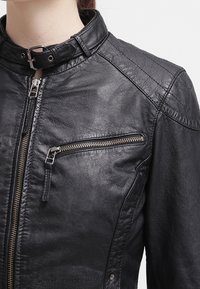 Svart läderjacka med ståkrage, framdragkedja och en dragkedjeförsedd bröstficka med silverdetaljer. Texturerad yta och sömnadsdetaljer.