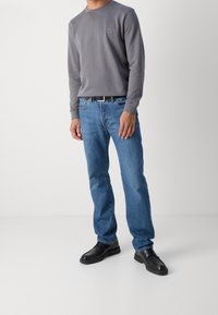 Szary długi rękaw sweatshirt z małym logo na piersi, połączony z jasnoniebieskimi spodniami typu straight-leg i czarnymi butami.