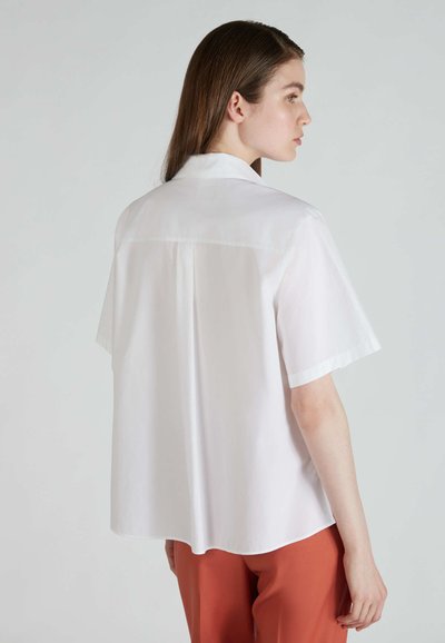 Camicia bianca a maniche corte con colletto classico, texture liscia e vestibilità rilassata, caratterizzata da una cucitura sul retro e un leggero lucido.