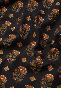 Sort stof med et gentaget mønster af orange og lilla blomster motiver med grønne accenter, blandet med små geometriske former.