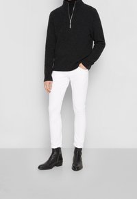 Sudadera negra con cremallera, vaqueros blancos ajustados y botas negras de tobillo. El conjunto presenta una textura suave y un corte clásico.