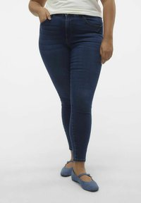 Vaqueros ajustados azul oscuro con una textura suave, cintura de media altura y diseño de cinco bolsillos, combinados con bailarinas azul claro.