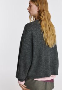 Szary wełniany sweter o pudełkowym kroju, szerokich rękawach i okrągłym dekolcie; założony na jasnoróżową koszulę i zieloną spódnicę.