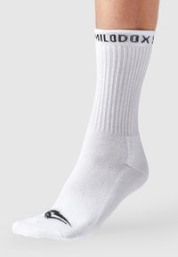 Calcetín deportivo blanco con textura acanalada que presenta un logo negro en la puntera y texto negro en el puño. El material tiene un aspecto suave y elástico.