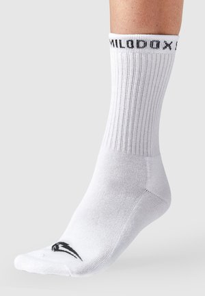 Witte geribbelde sportsocken met een zwart logo op de teen en zwarte tekst op de boord. Het materiaal lijkt soepel en rekbaar.