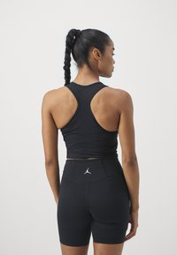 Top deportivo negro sin mangas con diseño de espalda nadadora, combinado con pantalones cortos negros de cintura alta que presentan un pequeño logo blanco en la parte trasera.